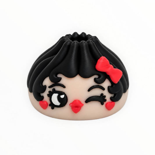 Wink & a Kiss 3D printed dumpling bead featuring black curly hair, a red bow, one winking eye, long eyelashes, red heart-shaped cheeks, and bright red lips.