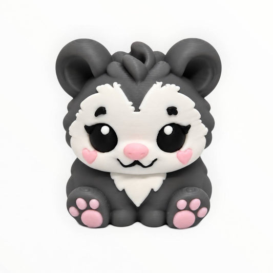Possum Blossom 3D printed possum bead featuring a cute sitting gray opossum with a white face, large black eyes, pink heart-shaped cheeks, pink nose, oversized ears, and pink paw pads.
